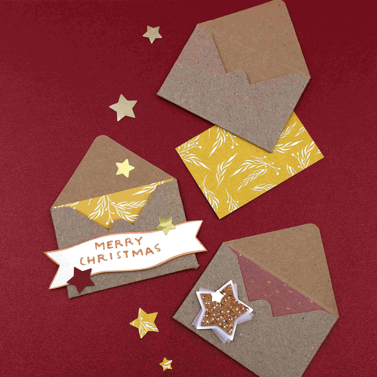 Drei kleine Geschenkkuverts der Firma Artoz Papier AG mit festlichen Einlagen und passenden Karten – ideal als Geschenkkuverts oder zur Verpackung von Gutscheinen – sind vor einem leuchtend roten Hintergrund angeordnet. Auf einer Karte steht „Merry Christmas“, während goldene Sterne und eine kleine sternförmige Schale voller Glitzer die Szene umgeben und ihr die Eleganz des Schweizer Designs verleihen.