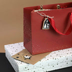 Un sac cadeau rouge à pois dorés et doté de poignées en ruban trône sur deux boîtes blanches ornées d'un motif d'étoiles issues de la collection « Boîte cadeau Pure A4, motif de Noël étoiles » de la société Artoz Papier AG, formant ainsi un emballage raffiné pour vos cadeaux d'exception. Une enveloppe marron, ornée d'étoiles et d'arbres, repose sur les boîtes et rend cet ensemble idéal pour une « boîte-cadeau Pure A4 » ou même comme élégant étui à livres.