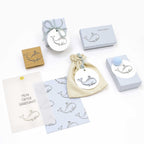 Un charmant coffret cadeau d'Artoz Papier AG comprenant des boîtes, une pochette à cordon et des cartes avec un adorable motif de baleine. Comprend le tampon Stempel Wal et une carte avec "MEIN ERSTER HAARSCHNITT" en allemand sur fond blanc.