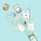 Ein blauer Hintergrund mit einer goldenen Schachtel und festlichen Partyutensilien wie Kerzen, Karten und Konfetti, die aus einem Artoz Papier AG Tischbombe ohne Feuer - "Happy Birthday" 3er Set, komplett mit schimmernden goldenen Luftschlangen, platzen.