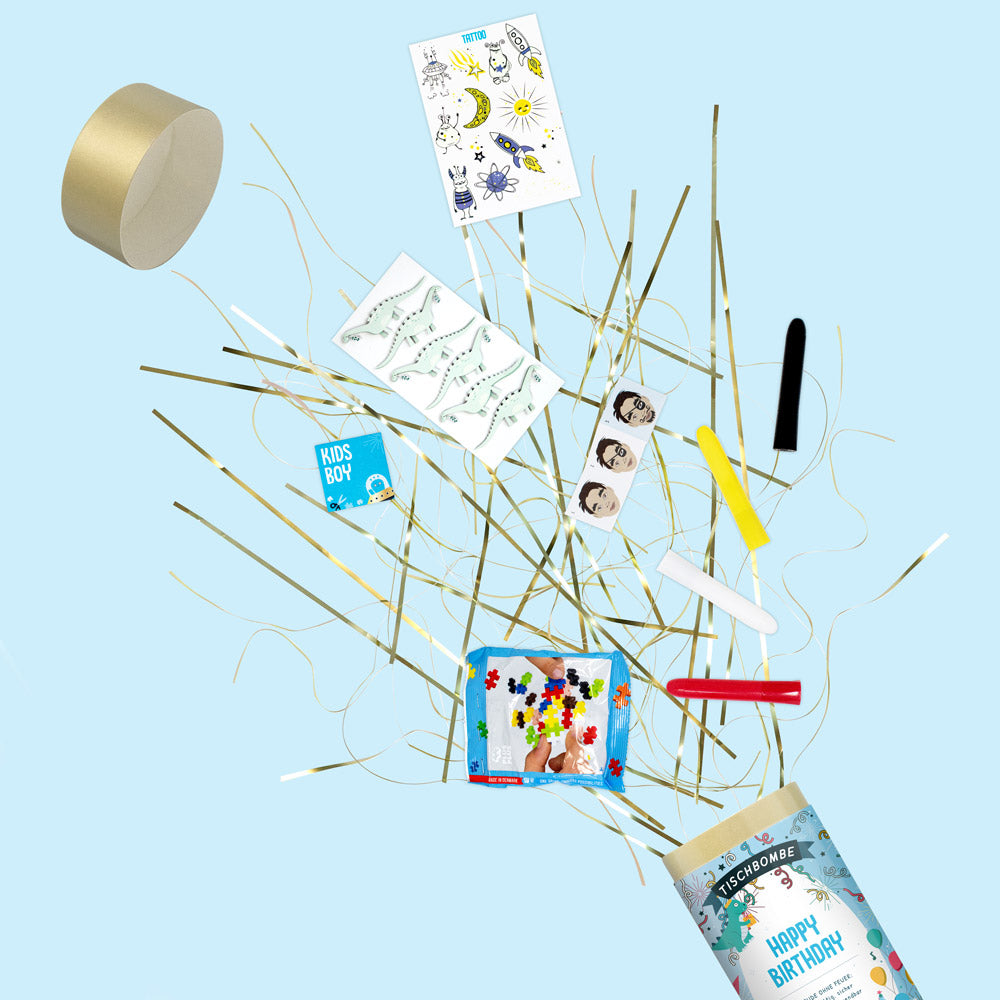 Le papier Artoz Papier AG "Tischbombe ohne Feuer - Happy Birthday Boy" éclate pour libérer des banderoles dorées, des autocollants, un bracelet, des crayons de couleur et une étiquette "Happy Birthday" sur un fond bleu clair.