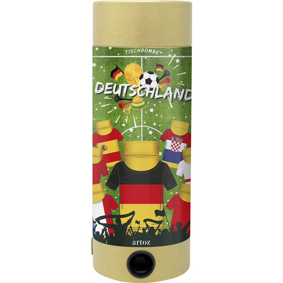 L'Artoz Papier AG Tischbombe ohne Feuer - Fussball WM Team Deutschland est un popper cylindrique décoré de ballons de football, d'éléments festifs et de maillots "DEUTSCHLAND" centrés sur un maillot noir, rouge et jaune de l'équipe sur fond vert.