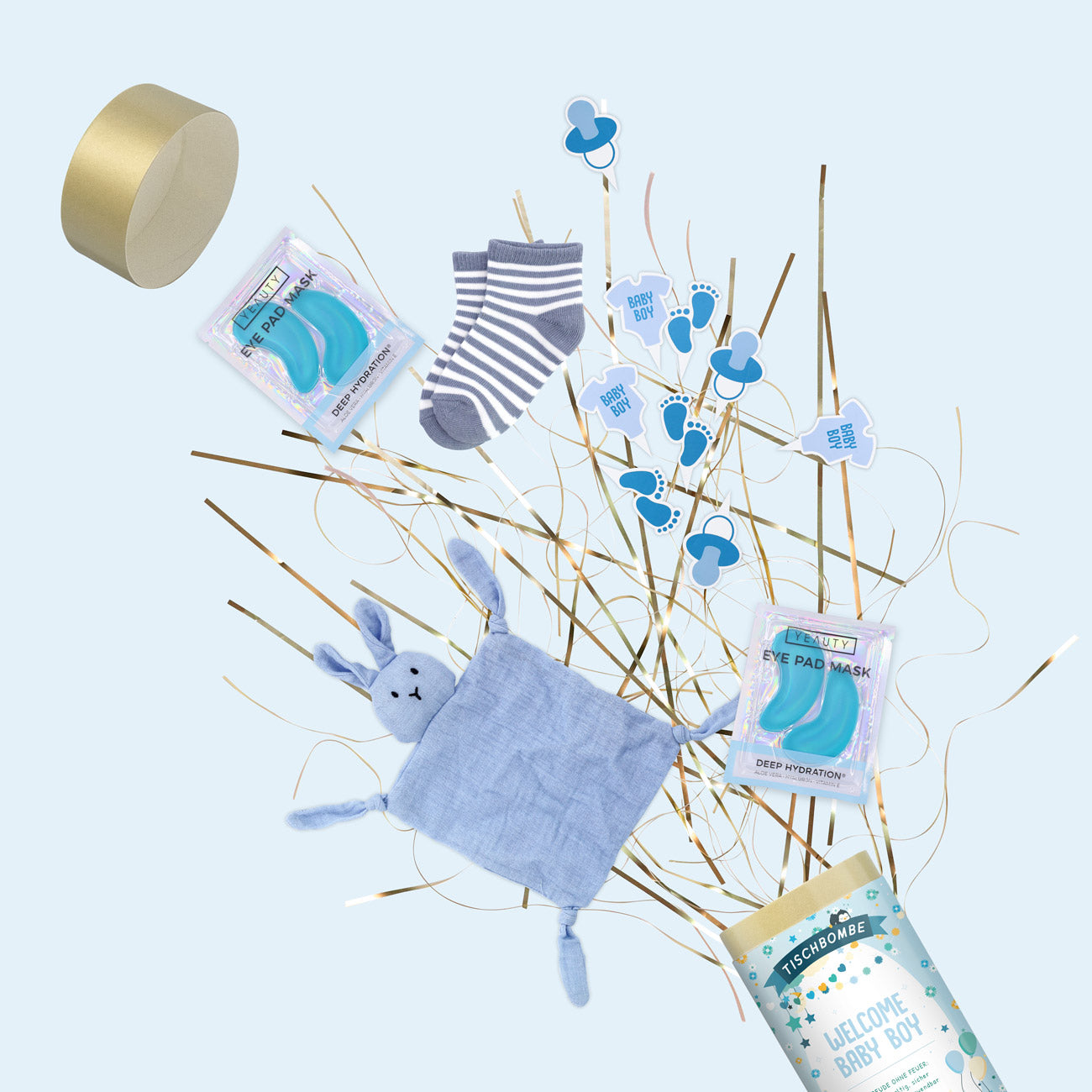 Un coffret cadeau pour bébé garçon comprenant des chaussettes rayées, un doudou lapin bleu, deux masques pour les yeux, des pics bleus "Welcome Baby Boy", un savon de bain "Welcome Baby Boy" sur des bâtonnets dorés et blancs, et un Artoz Papier AG Tischbombe ohne Feuer - le tout sur un fond bleu clair.