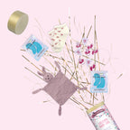 Un coffret cadeau pour bébé sur fond rose avec décor doré, comprenant un lapin tout doux, des chaussettes pour bébé, des masques hydratants pour les yeux, des autocollants, un message Artoz Papier AG Tischbombe ohne Feuer - Welcome Baby Girl, et un couvercle de boîte ronde dorée.